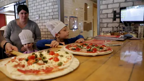 Two children in chef hats with the pizzas they topped at Square Peg